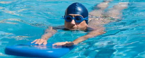 man in swimming pool with a float, goggles and swimming hat